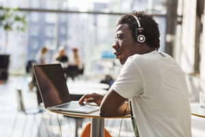 Male college student looking away while listening music through laptop at cafe